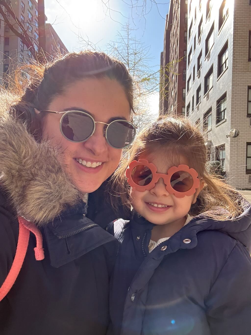 Mom and daughter on a sunny city street, both in sunglasses